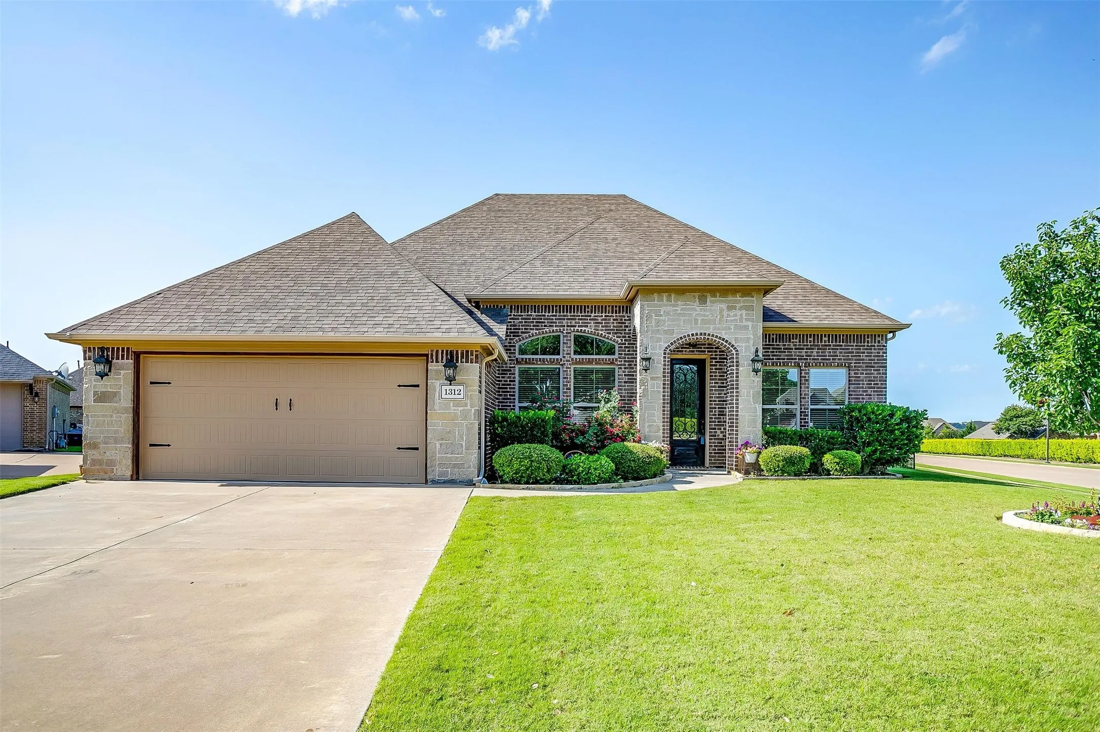 French country style house featuring a shingled roof, a front yard, driveway, a garage, and brick siding