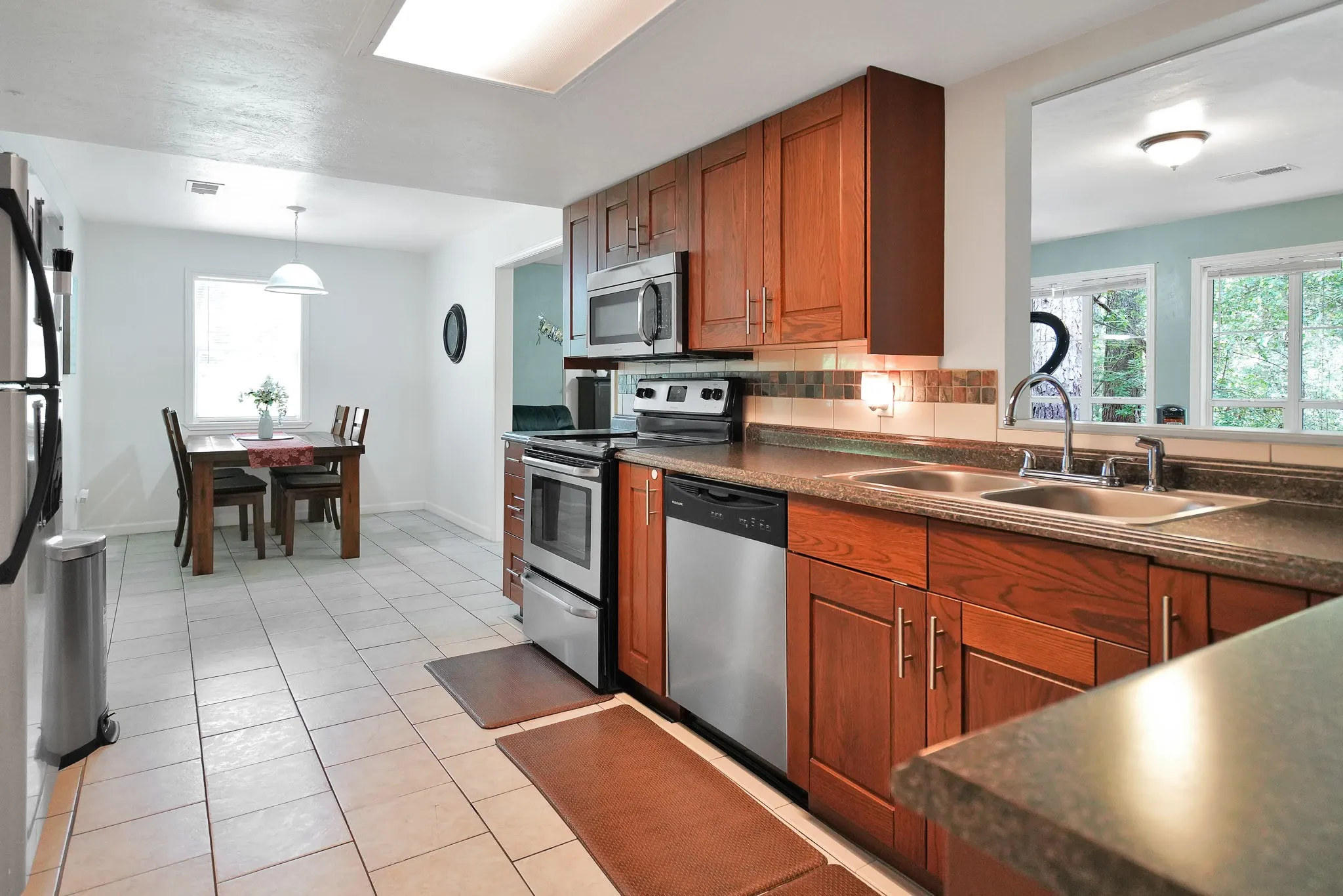 Kitchen featuring appliances with stainless steel finishes, dark countertops, brown cabinetry, decorative backsplash, and light tile patterned floors