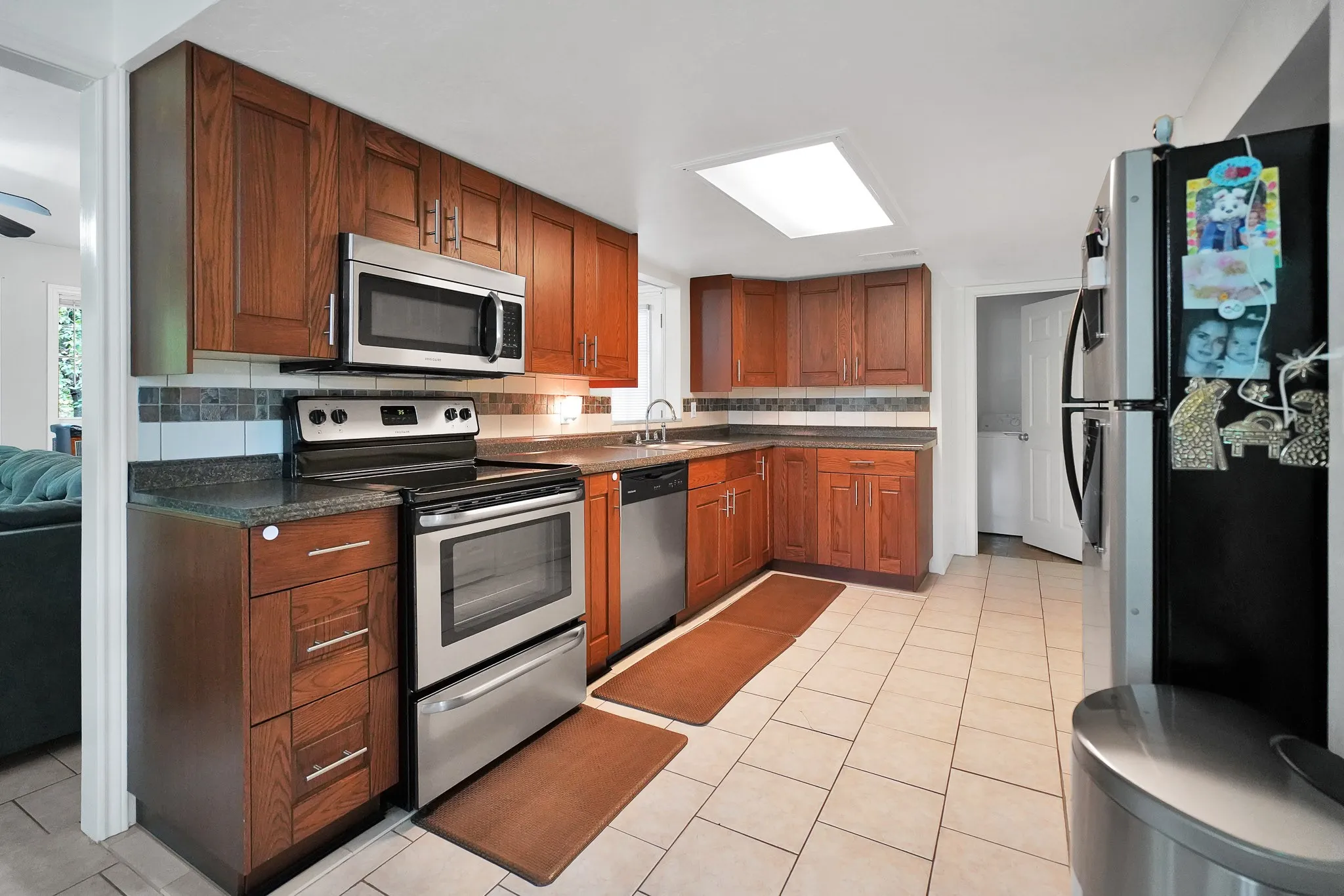Kitchen featuring appliances with stainless steel finishes, tasteful backsplash, dark countertops, and light tile patterned flooring