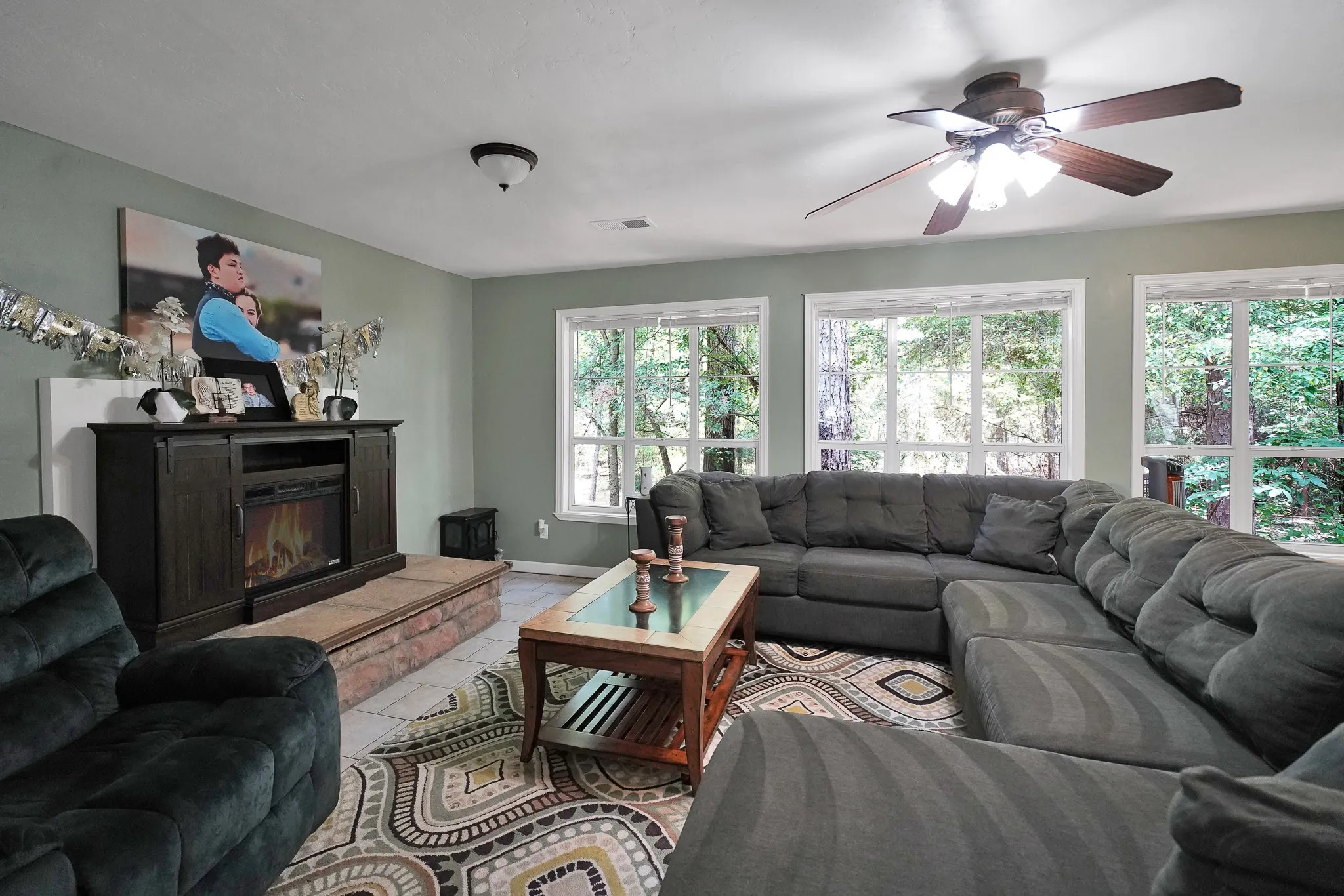 Living room with a ceiling fan, light tile patterned floors, and a glass covered fireplace