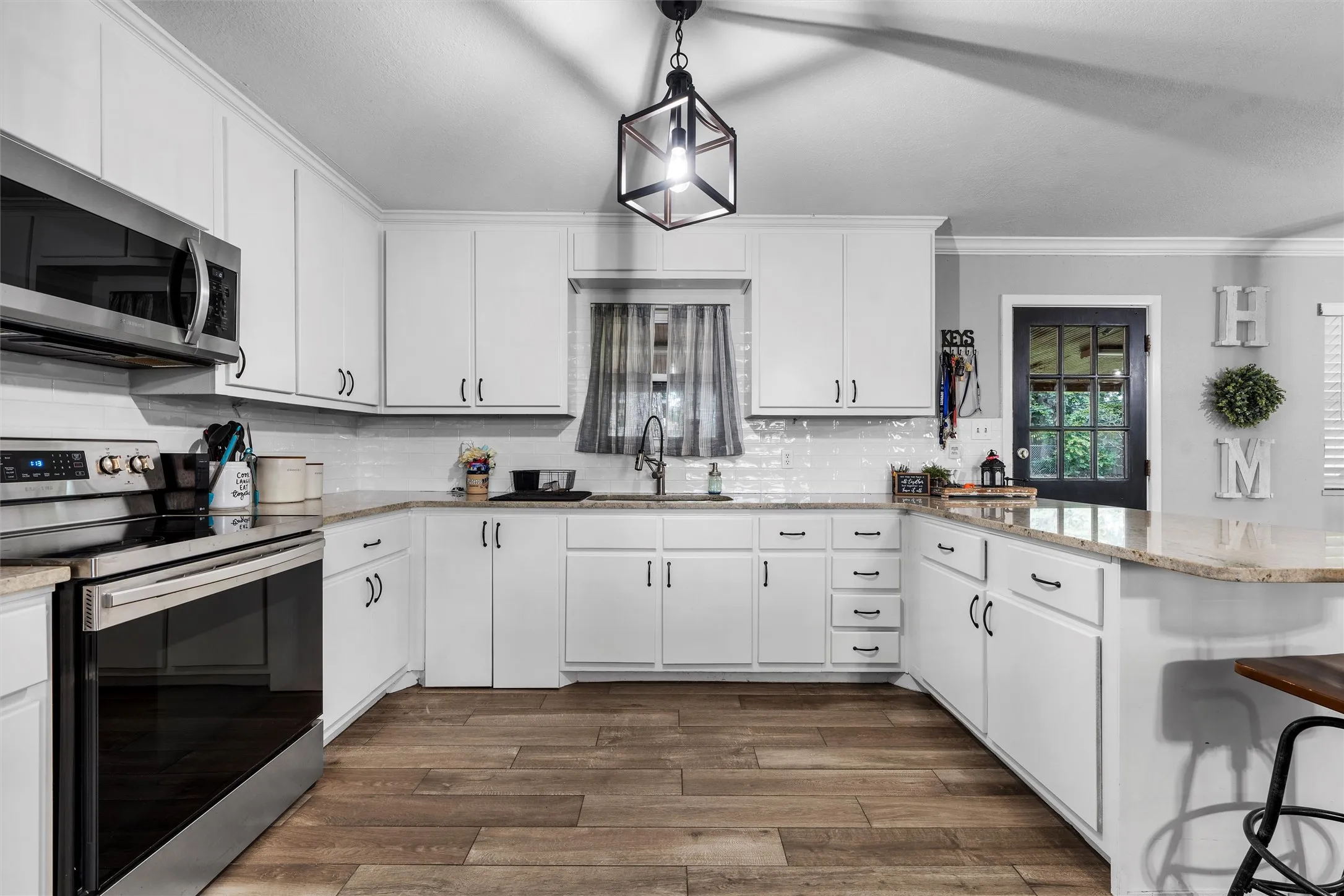 Kitchen with appliances with stainless steel finishes, a peninsula, crown molding, dark wood-style floors, and white cabinetry