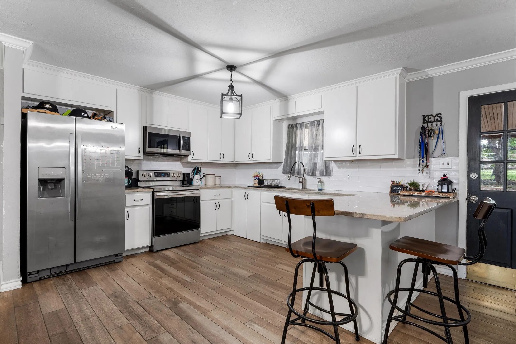 Kitchen featuring appliances with stainless steel finishes, a peninsula, wood finished floors, decorative backsplash, and ornamental molding