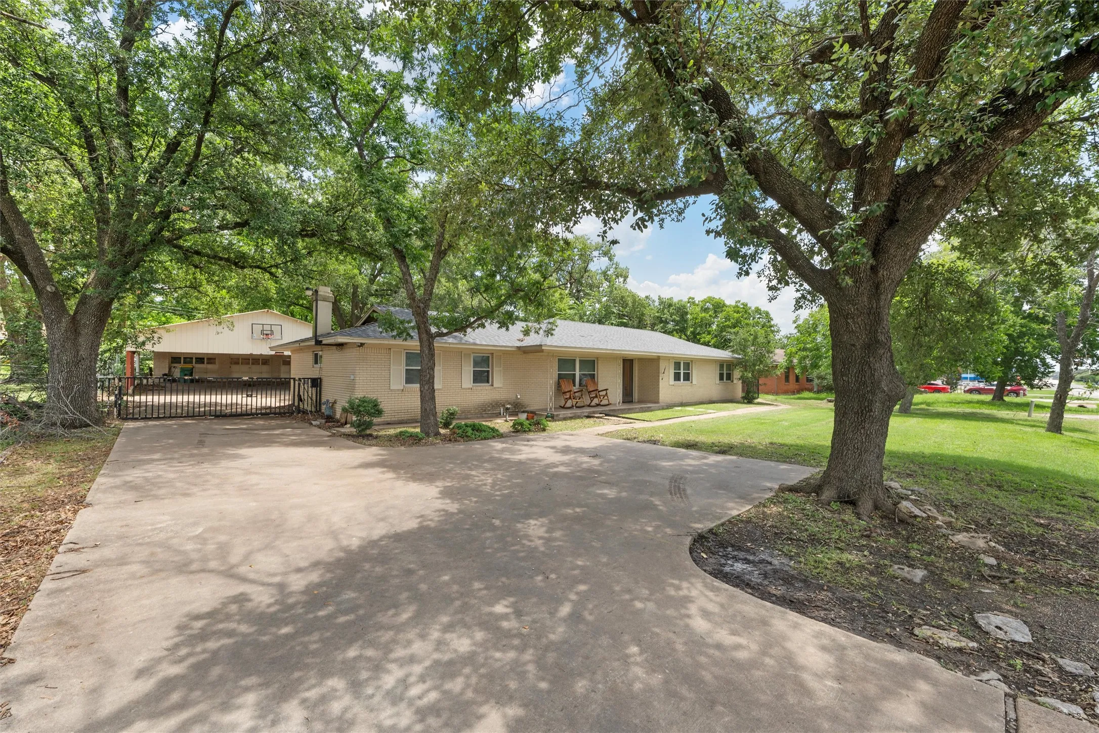Single story home featuring a gate, driveway, a chimney, and brick siding