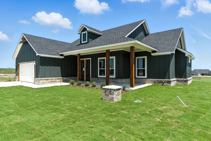 View of front of house featuring board and batten siding, roof with shingles, a garage, and a front yard