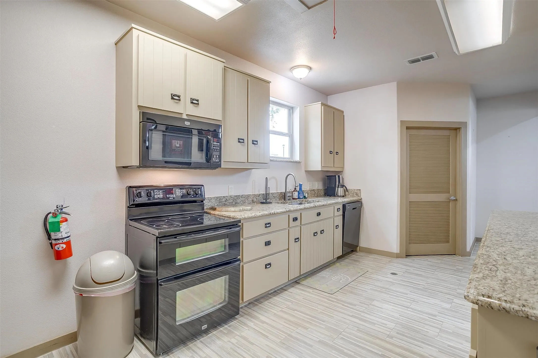 EVENTER CENTER- Alternate view of Kitchen with serving counter, lots of storage, light wood-style floors and emergency exit.