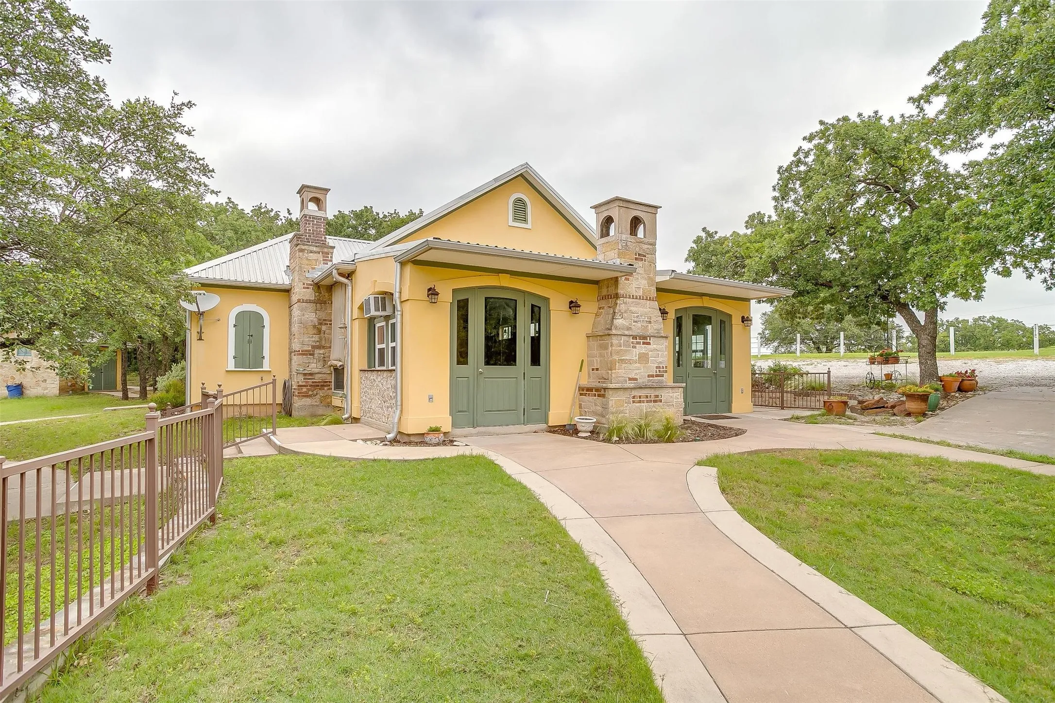 EVENT CENTER ALT VIEW of building hidden behind natural elements featuring driveway, stone siding, stucco siding, and a gazebo