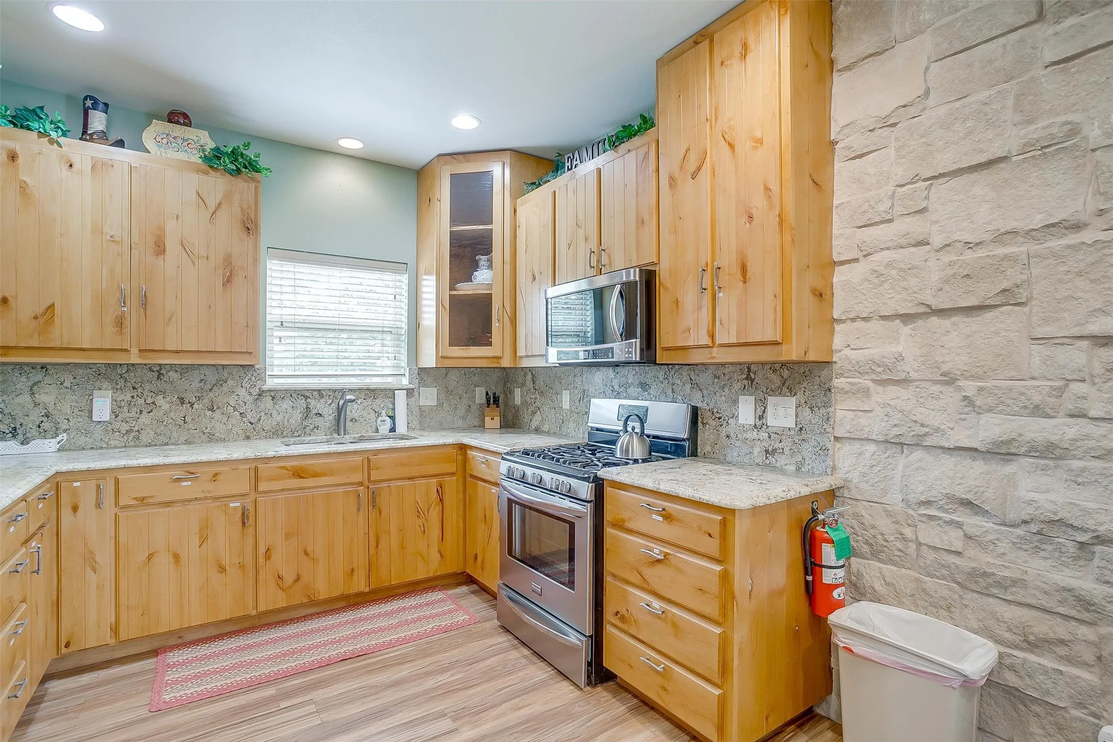 Still Water Cabin- Kitchen featuring appliances with stainless steel finishes, light wood-style floors, light brown cabinets, glass insert cabinets, and decorative backsplash