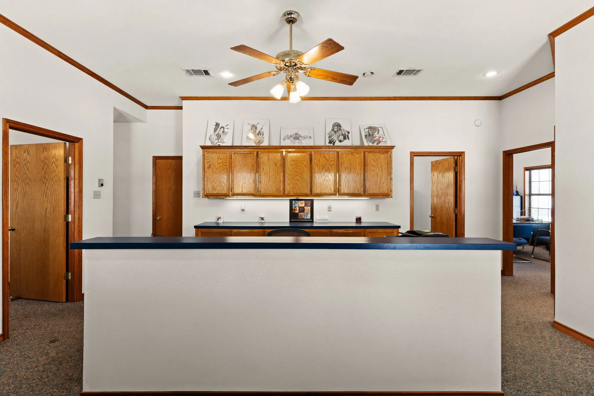 Kitchen with carpet flooring, crown molding, brown cabinetry, a ceiling fan, and dark countertops