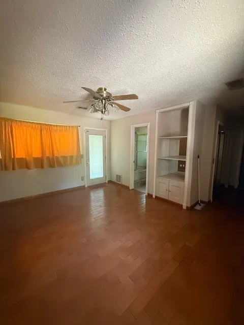 Unfurnished room with a textured ceiling, ceiling fan, wood finished floors, and built in shelves