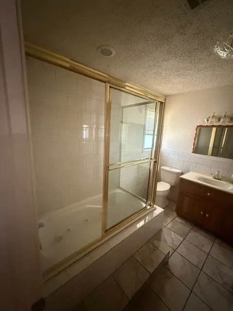 Full bath featuring a combined bath / shower with jetted tub, a textured ceiling, vanity, and tile walls