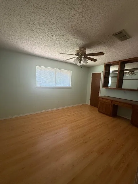 Unfurnished bedroom featuring built in desk, light wood-style floors, a textured ceiling, and ceiling fan