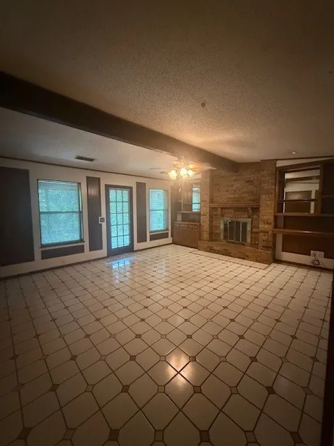 Unfurnished living room featuring a textured ceiling, plenty of natural light, and a brick fireplace