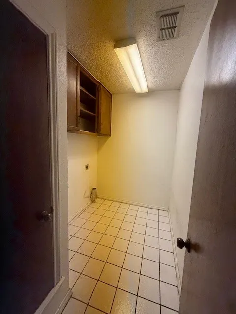 Laundry room featuring electric dryer hookup, a textured ceiling, and light tile patterned floors