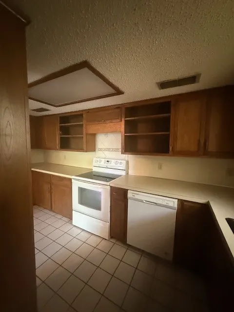 Kitchen featuring white appliances, open shelves, a textured ceiling, light tile patterned floors, and brown cabinets
