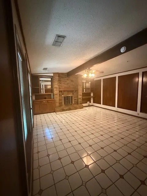 Unfurnished living room featuring a textured ceiling, a brick fireplace, built in shelves, and ceiling fan