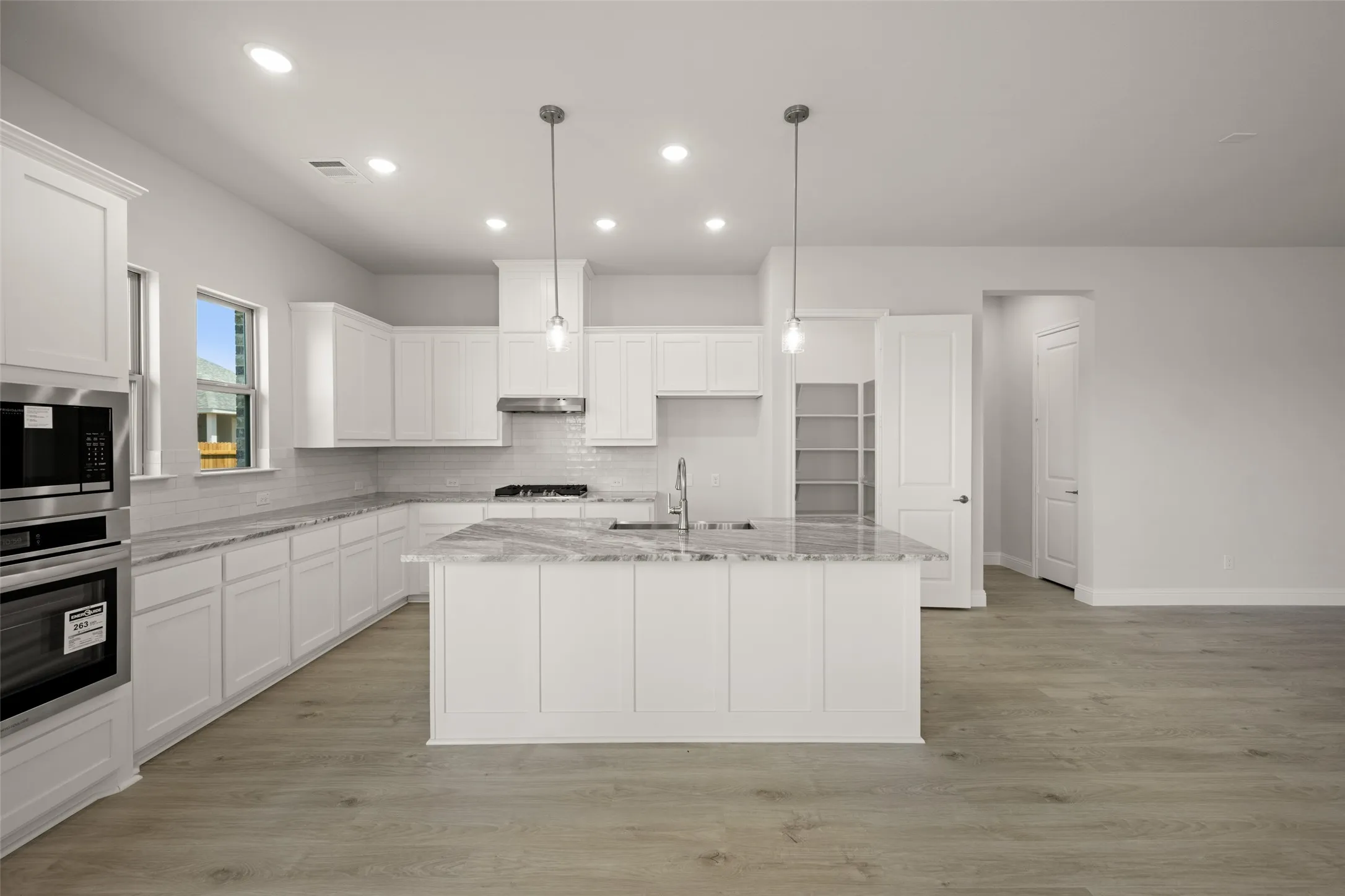 Kitchen with stainless steel appliances, white cabinets, backsplash, a center island with sink, and recessed lighting