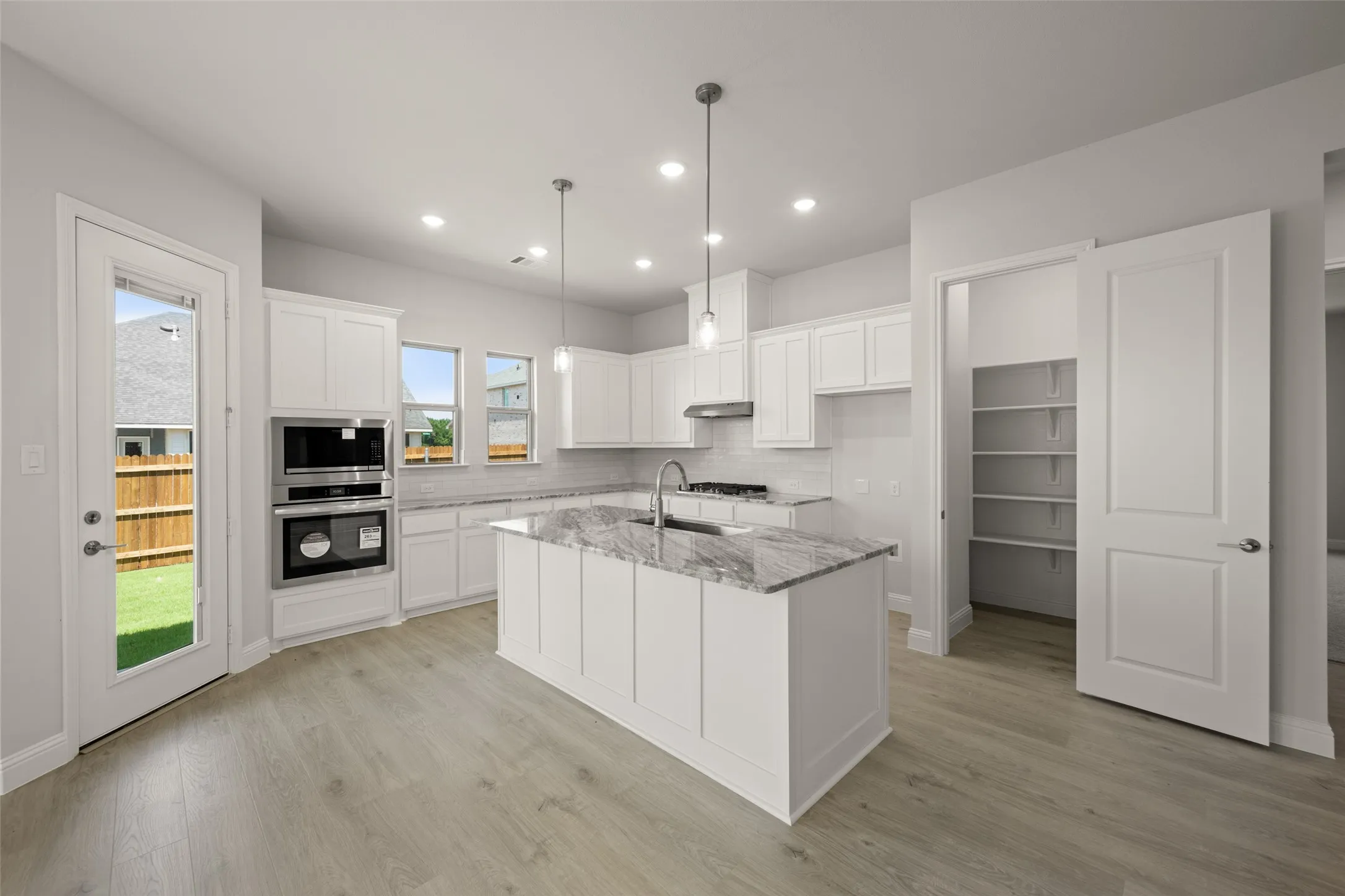 Kitchen with under cabinet range hood, tasteful backsplash, light stone countertops, white cabinets, and an island with sink