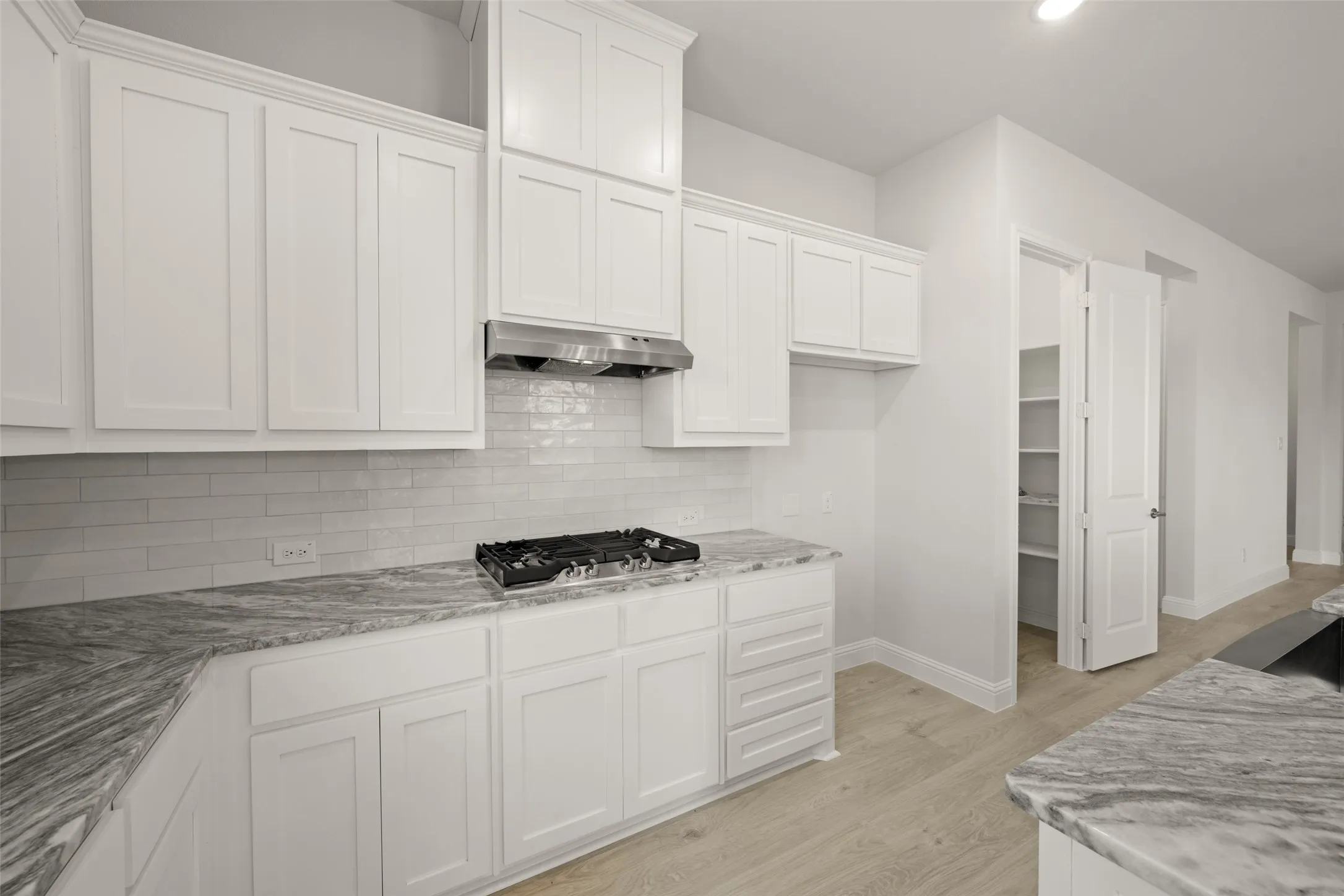 Kitchen with exhaust hood, stainless steel gas cooktop, white cabinets, and light wood-type flooring