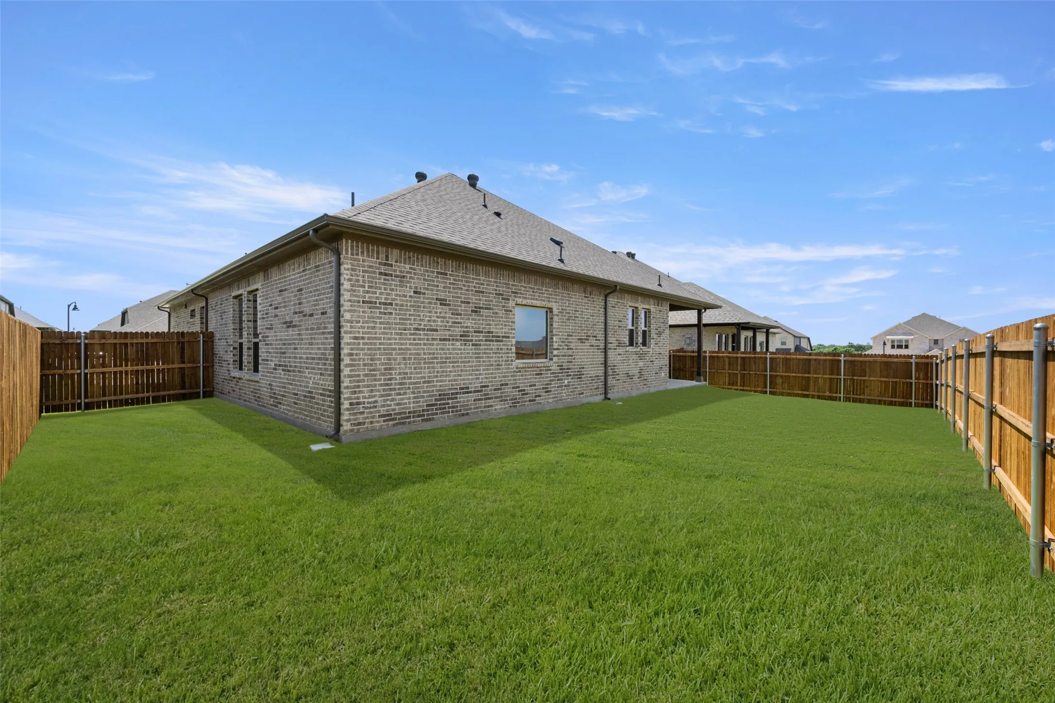 Back of house featuring brick siding, a fenced backyard, and roof with shingles