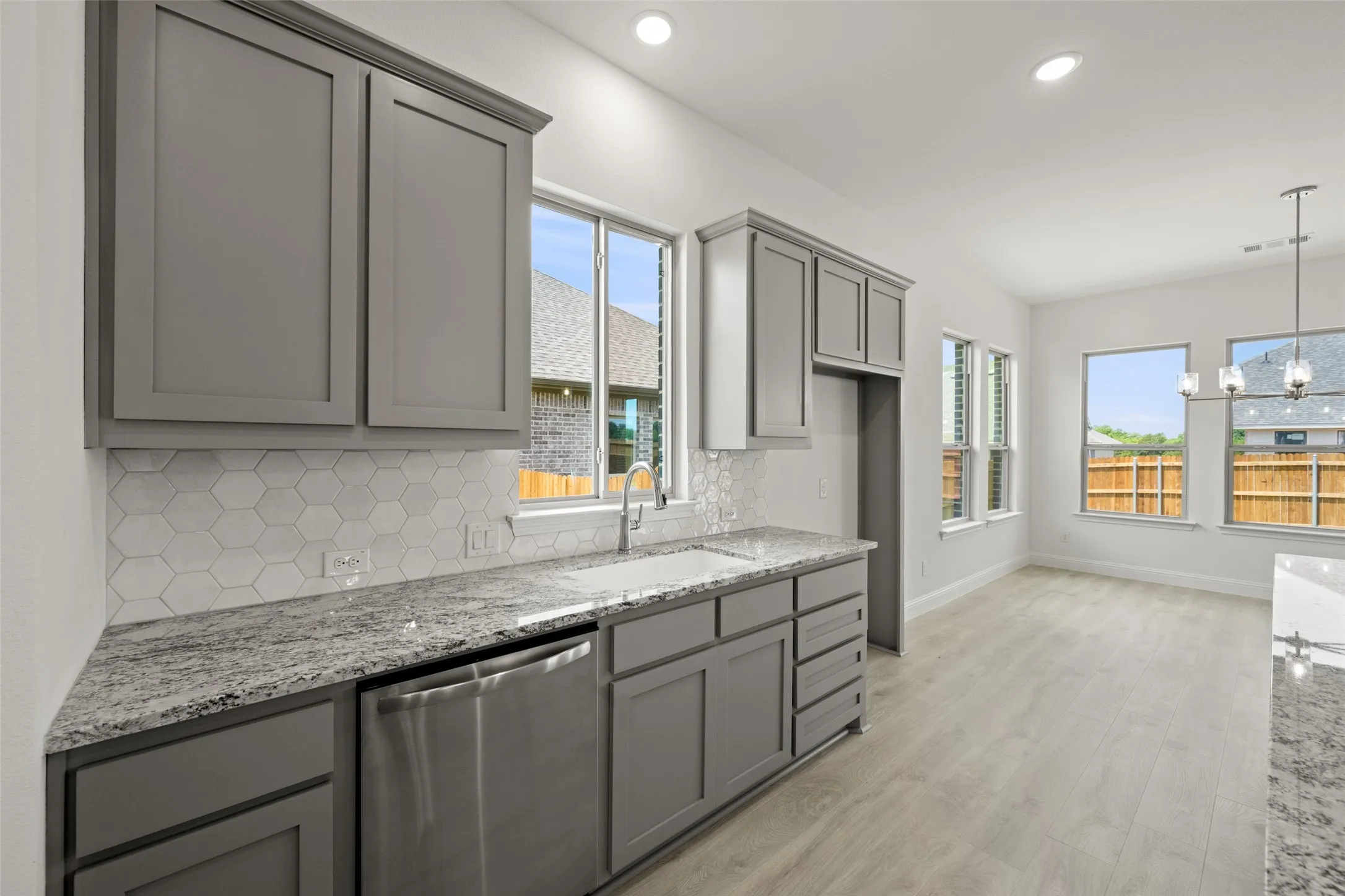 Kitchen with stainless steel dishwasher, gray cabinets, decorative backsplash, light stone counters, and recessed lighting