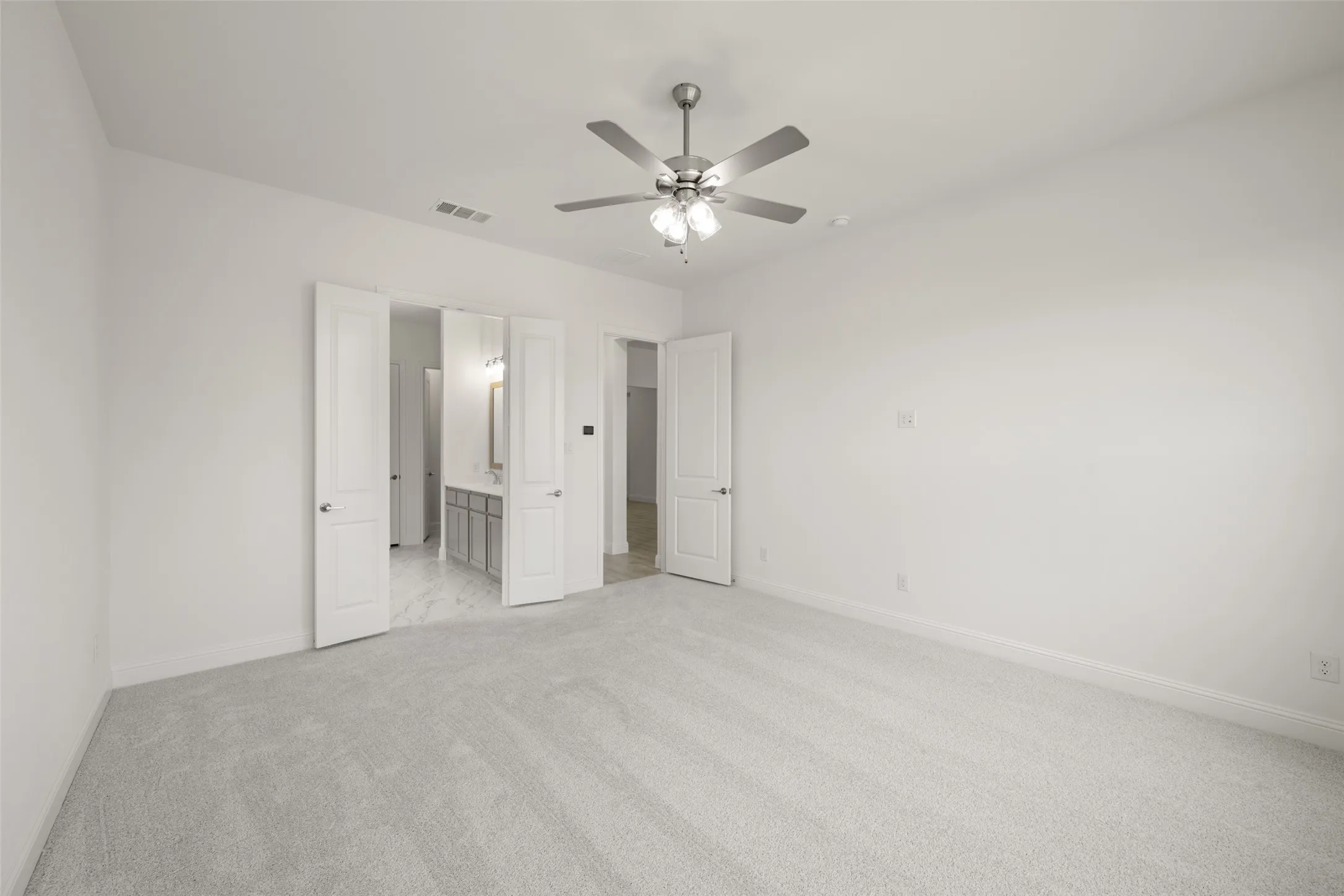 Unfurnished bedroom featuring light carpet, ensuite bath, and ceiling fan