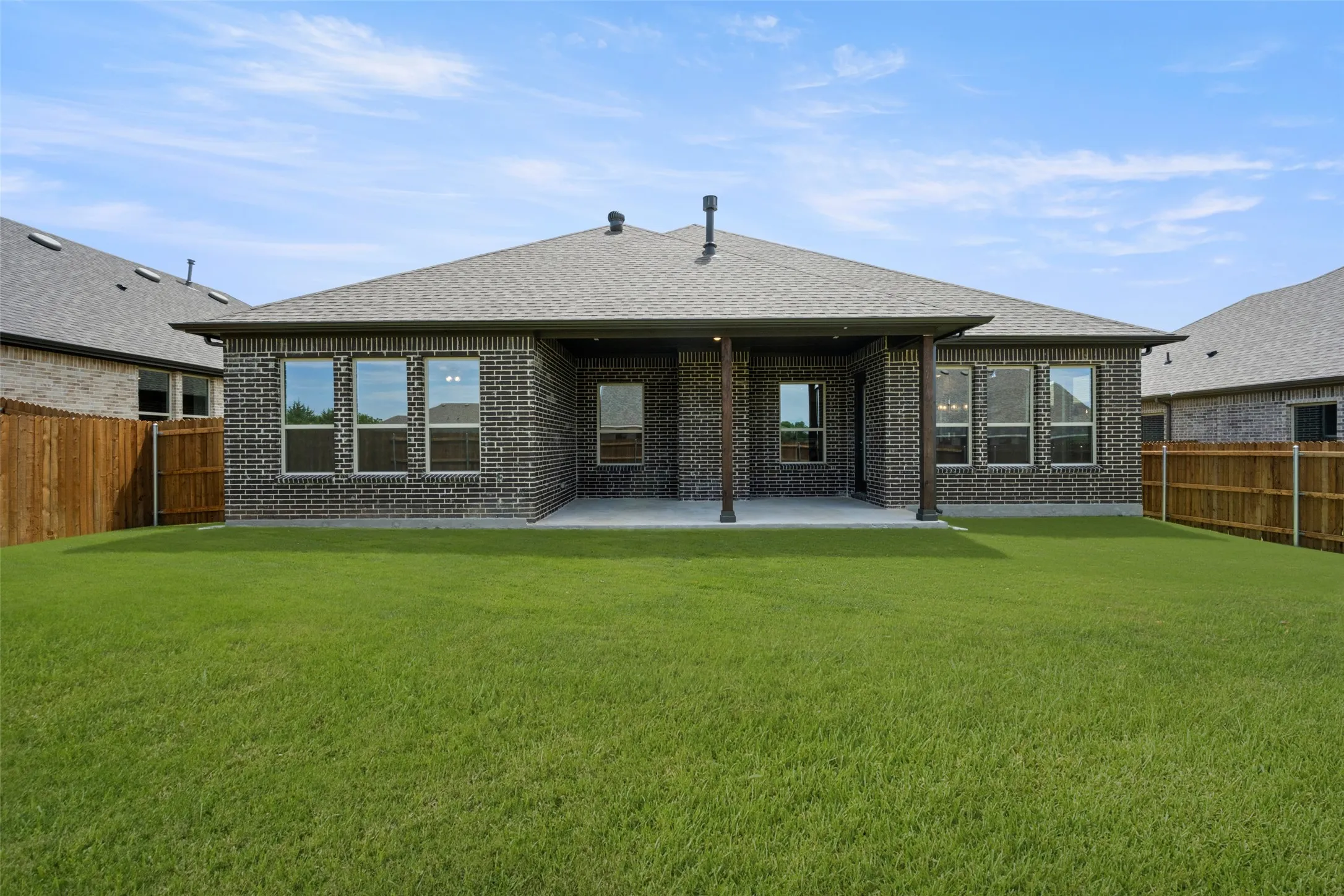 Rear view of property featuring brick siding, a fenced backyard, a patio, and roof with shingles