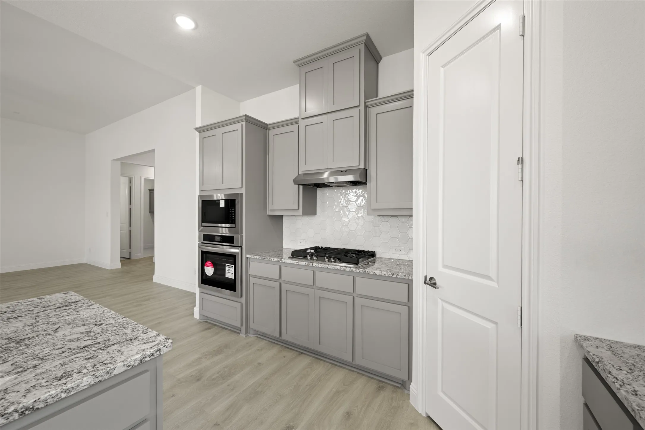 Kitchen with gray cabinetry, stainless steel appliances, under cabinet range hood, decorative backsplash, and light wood-style floors
