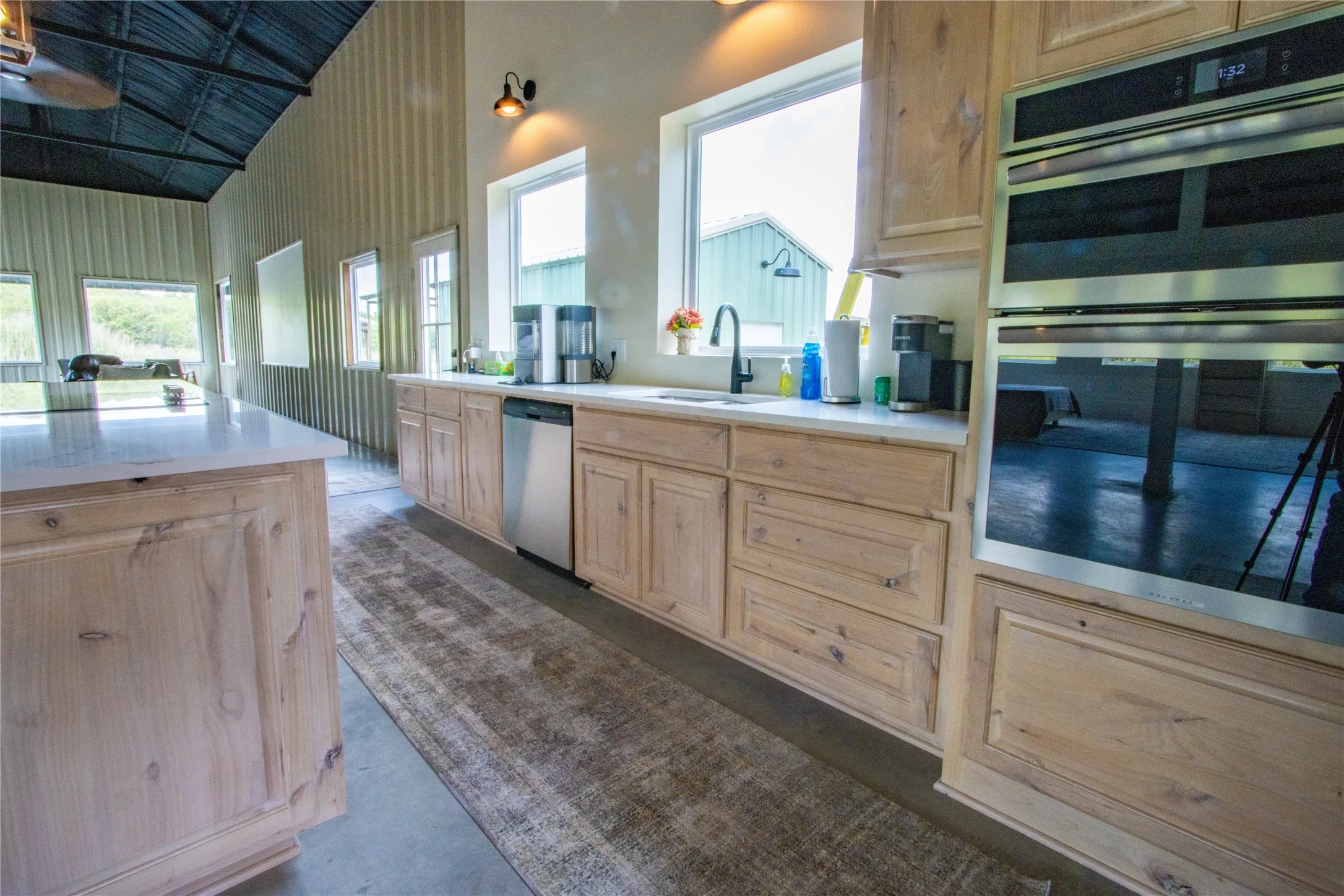 Kitchen featuring stainless steel appliances, light brown cabinetry, light countertops, finished concrete floors, and high vaulted ceiling