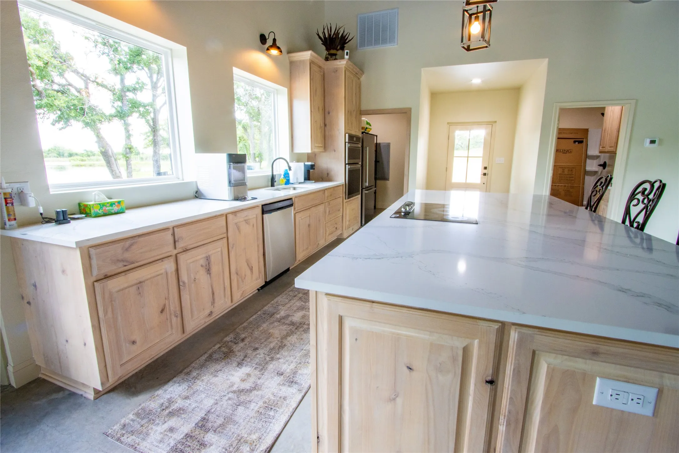 Kitchen featuring light brown cabinets, stainless steel dishwasher, black electric cooktop, a kitchen island, and pendant lighting