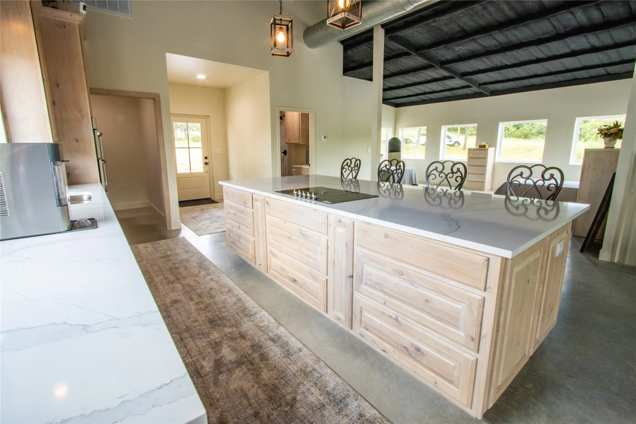 Kitchen featuring black electric cooktop, light brown cabinetry, a towering ceiling, a center island, and light stone countertops