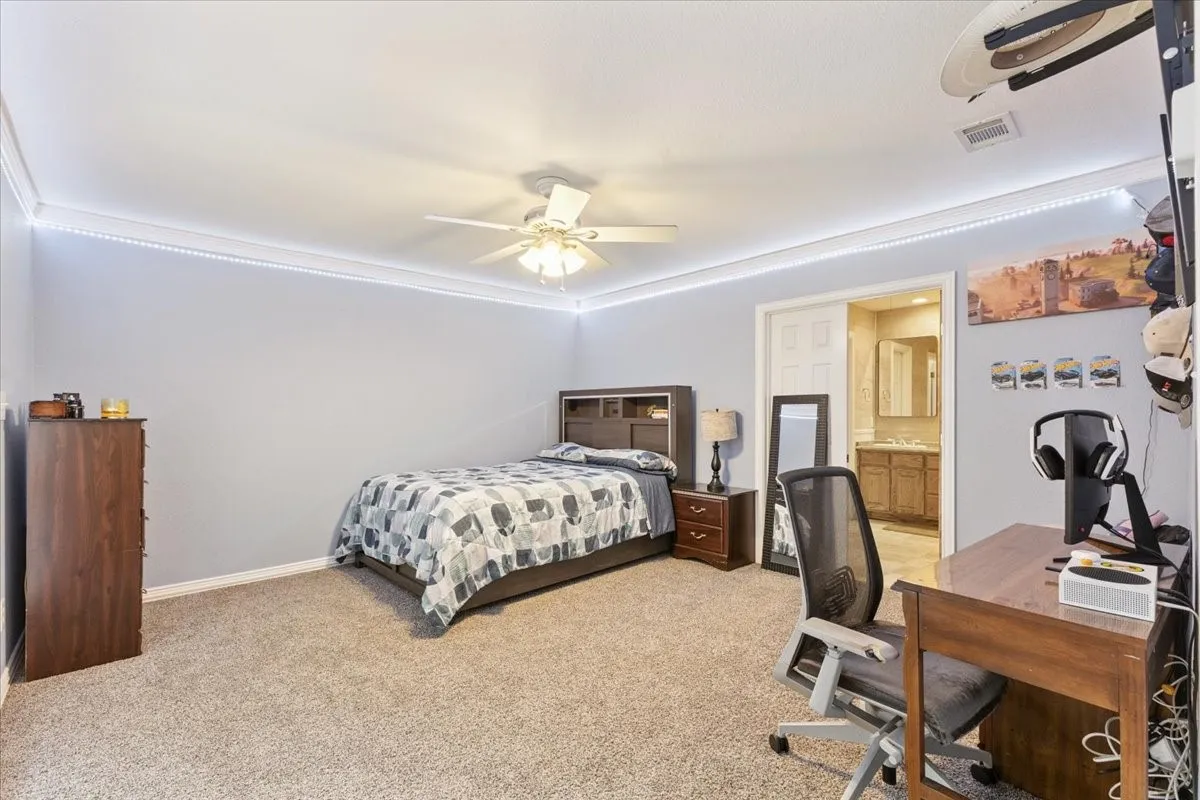 Bedroom with a desk, light carpet, a ceiling fan, and ensuite bathroom