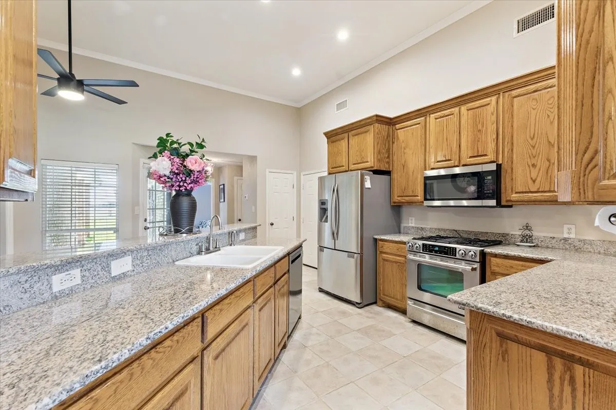 Kitchen featuring appliances with stainless steel finishes, ceiling fan, light tile patterned flooring, light stone countertops, and crown molding