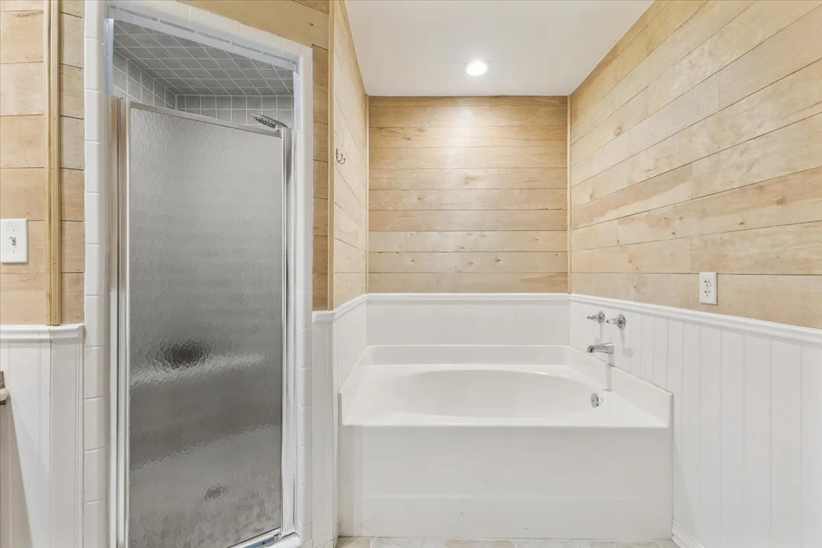 Full bath with wooden walls, a shower stall, a bath, and wainscoting