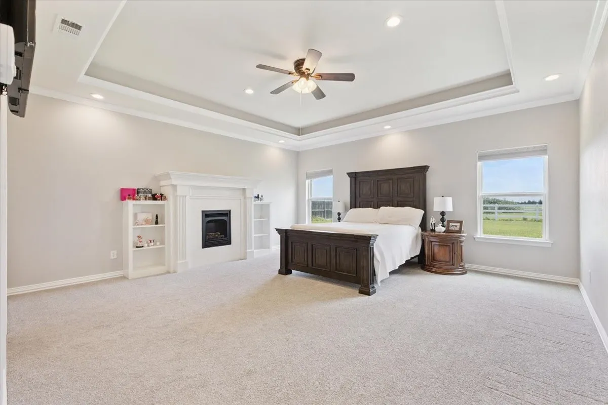 Carpeted bedroom featuring a tray ceiling, multiple windows, recessed lighting, a fireplace, and ornamental molding
