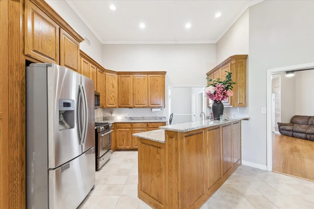Kitchen featuring stainless steel appliances, a peninsula, light stone countertops, crown molding, and brown cabinets