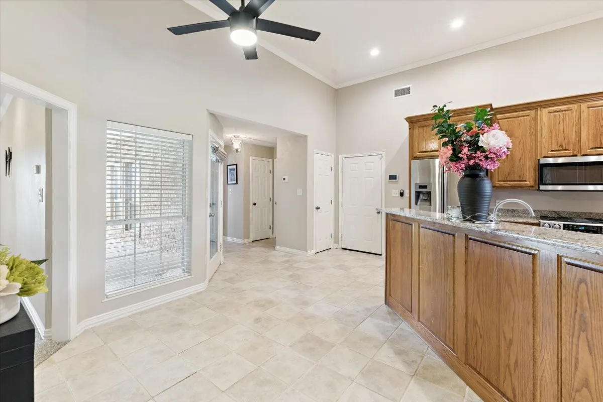 Kitchen with appliances with stainless steel finishes, light stone countertops, a ceiling fan, ornamental molding, and a towering ceiling