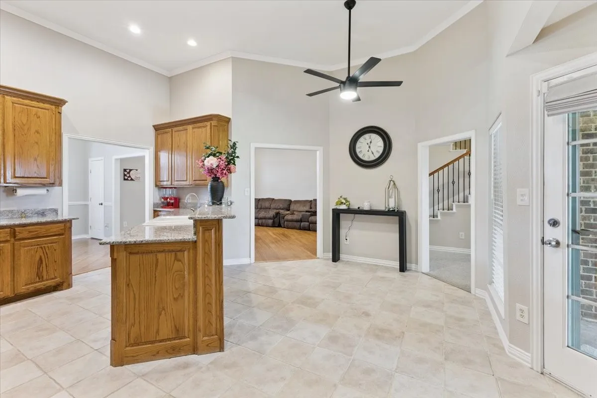 Kitchen featuring a towering ceiling, ceiling fan, brown cabinets, light stone counters, and crown molding