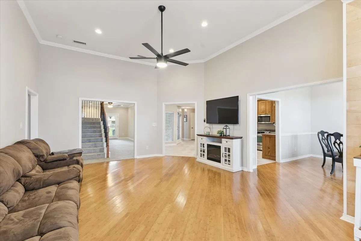 Living area with light wood-type flooring, a ceiling fan, stairway, a high ceiling, and ornamental molding