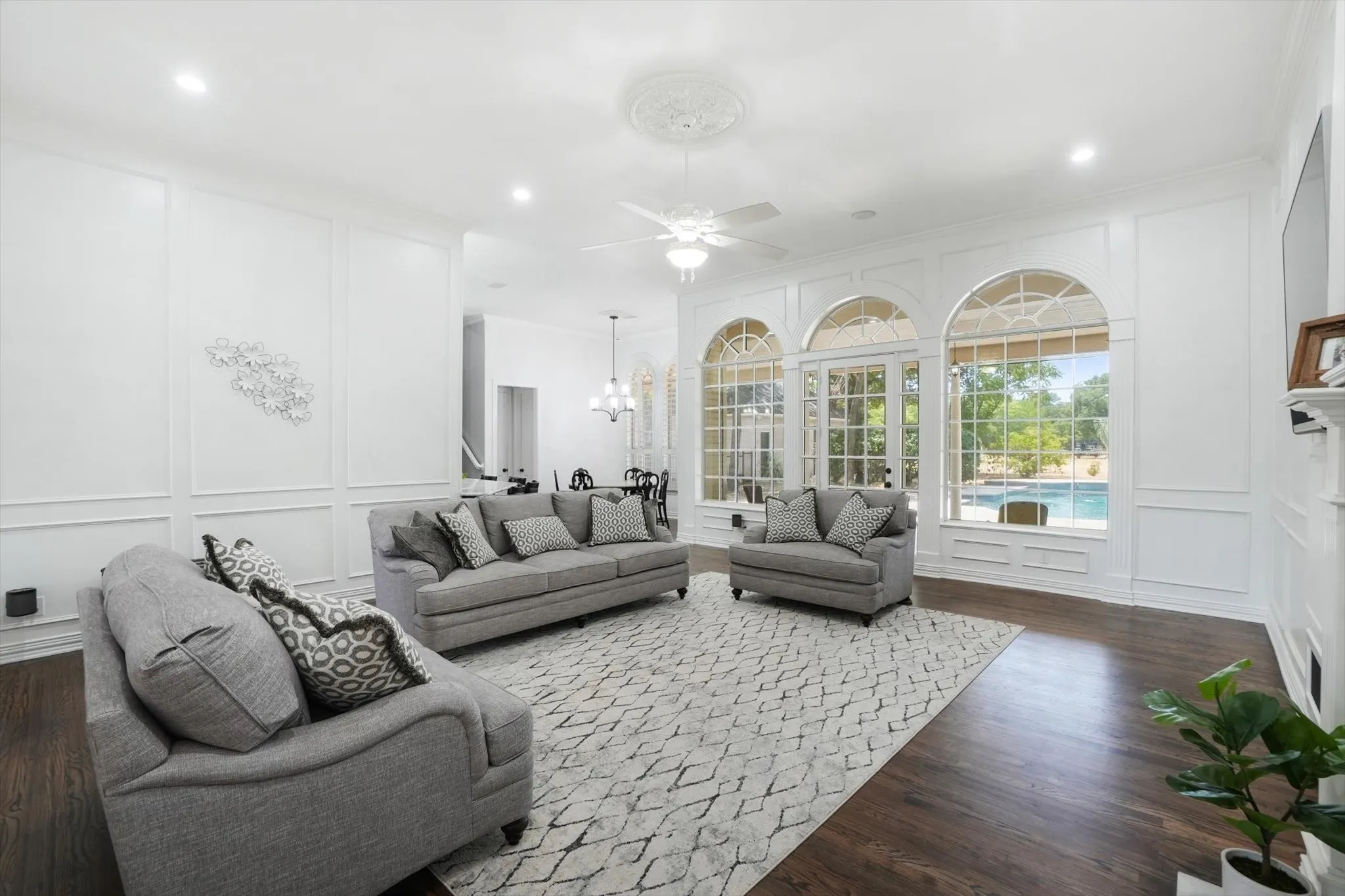 Living area with a decorative wall, dark wood-style floors, a ceiling fan, ornamental molding, and a chandelier