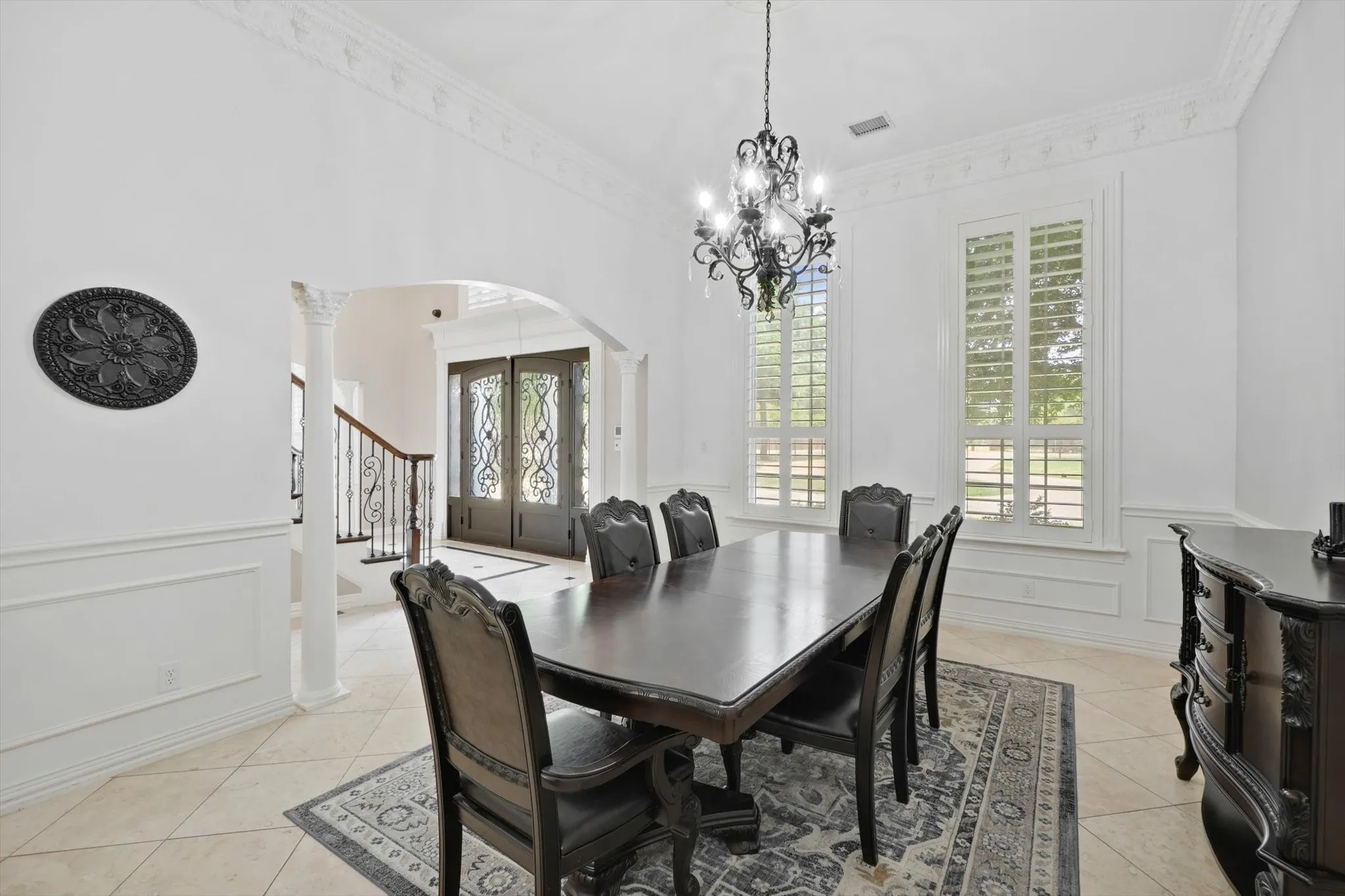 Dining room featuring arched walkways, light tile patterned flooring, a chandelier, a wainscoted wall, and a decorative wall