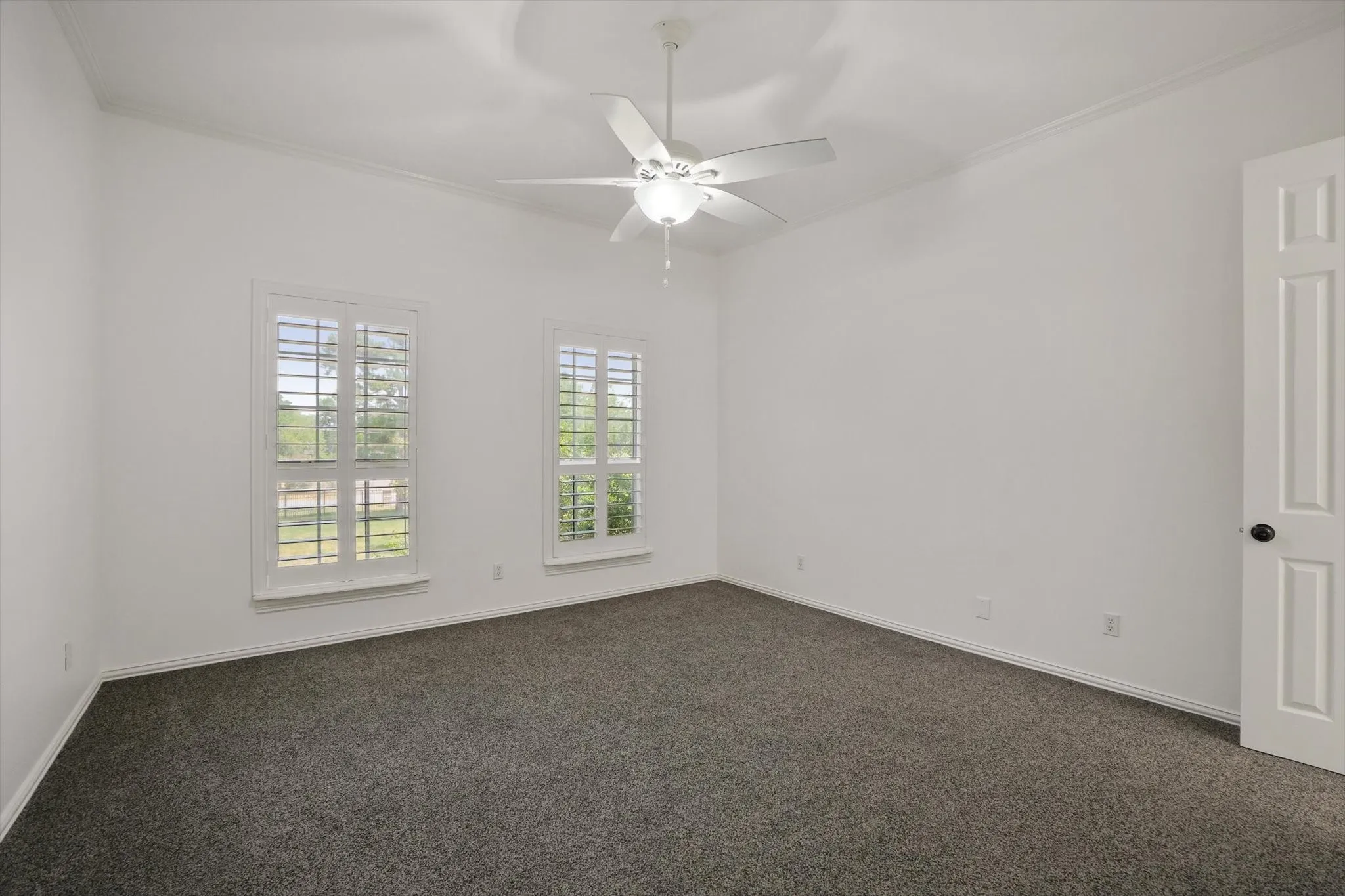Spare room featuring dark carpet, ornamental molding, and ceiling fan