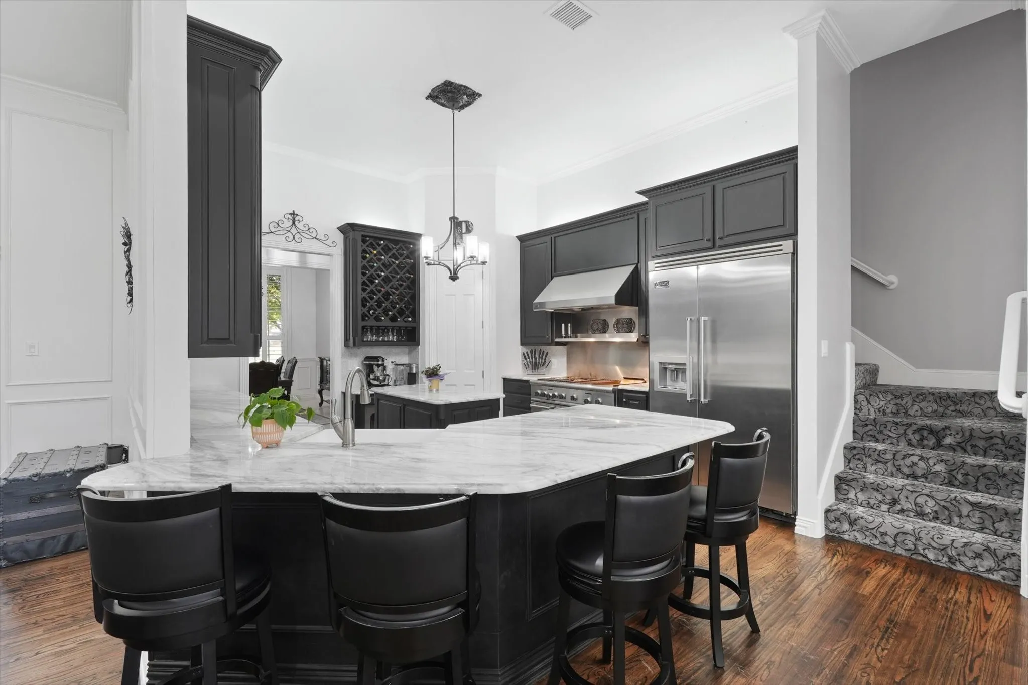 Kitchen featuring high end appliances, under cabinet range hood, dark wood-style flooring, light stone counters, and ornamental molding