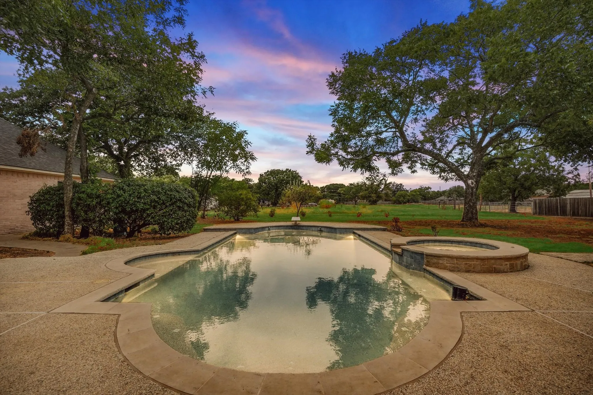 Pool at dusk featuring a pool with connected hot tub and a patio area