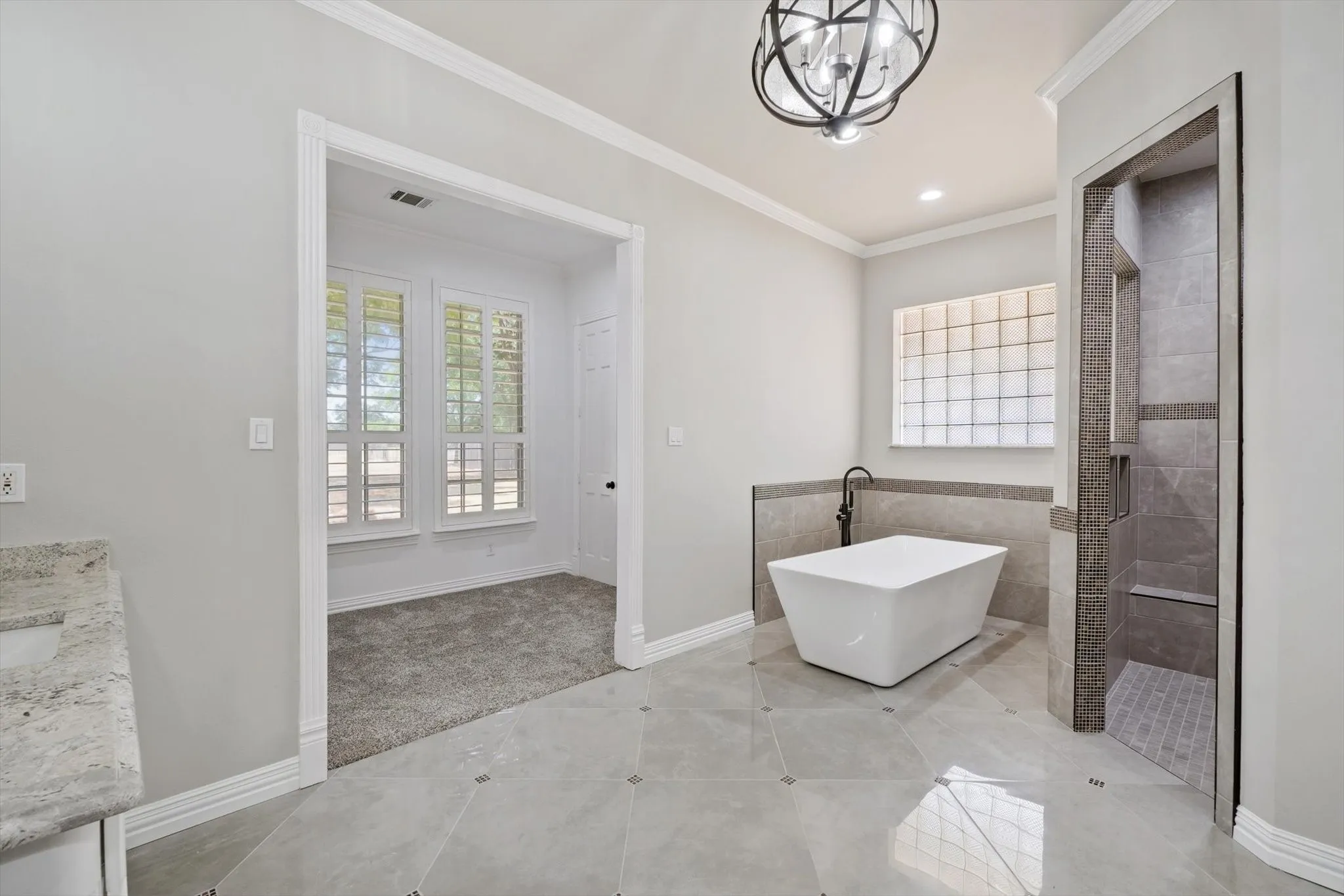 Full bath featuring a freestanding bath, plenty of natural light, a chandelier, crown molding, and a tile shower