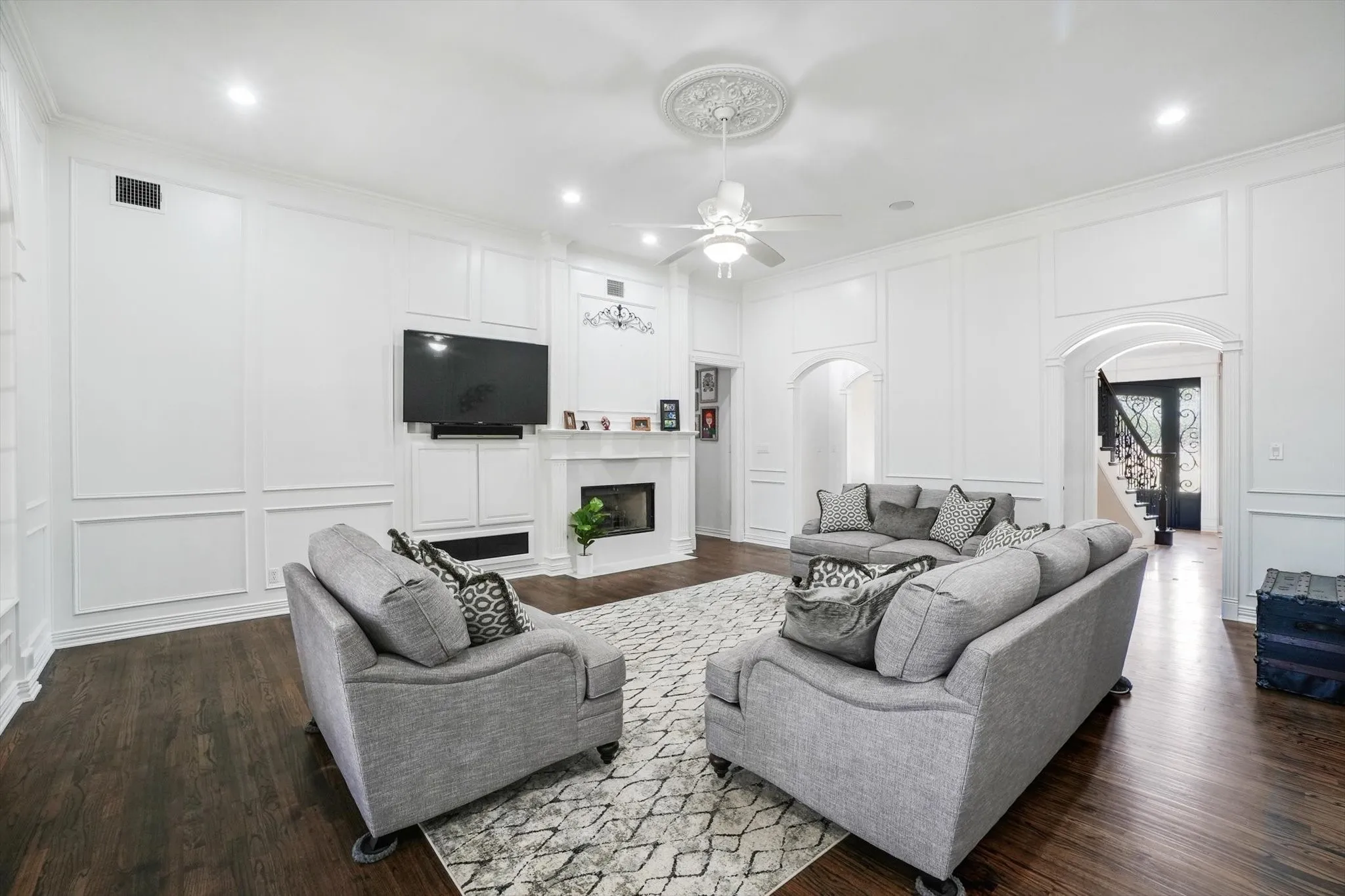 Living area with a decorative wall, arched walkways, a ceiling fan, ornamental molding, and stairs