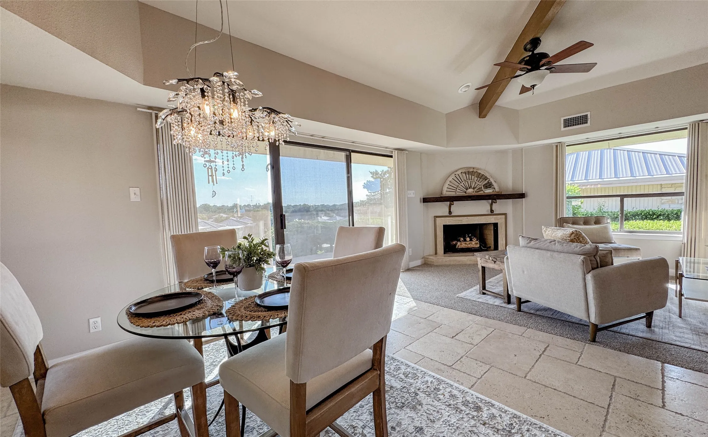 Dining room featuring stone tile floors, a chandelier, a fireplace with raised hearth, a ceiling fan, and beamed ceiling
