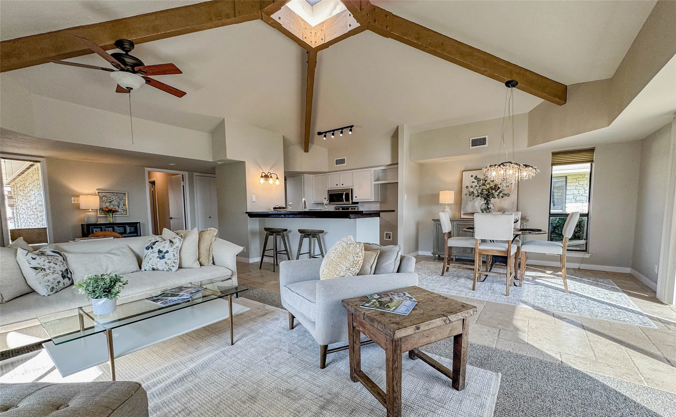 Living room featuring high vaulted ceiling, ceiling fan, beam ceiling, a chandelier, and stone tile flooring