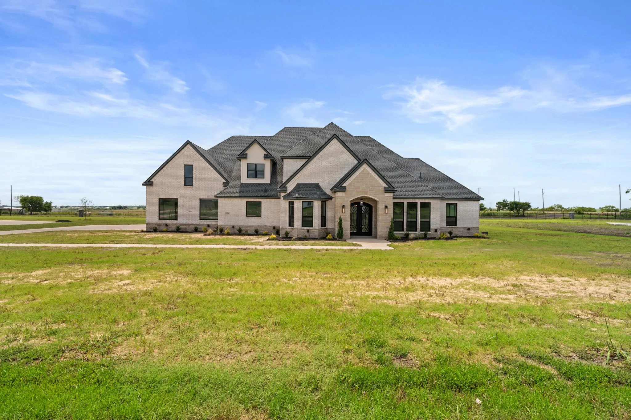 French country inspired facade featuring a front yard, a shingled roof, and brick siding