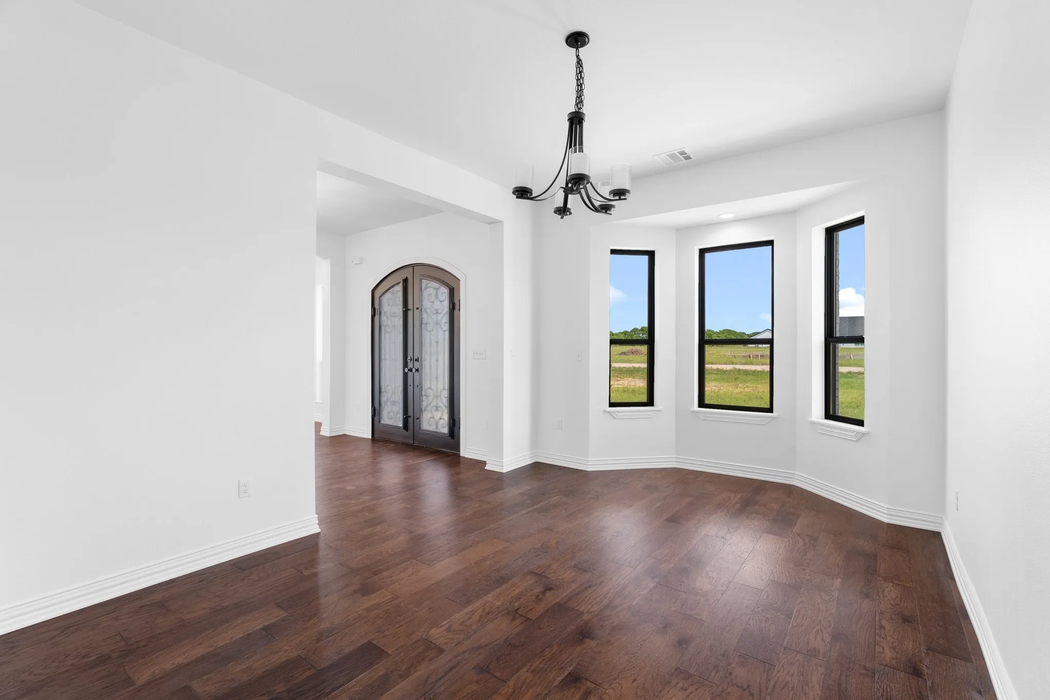 Empty room with a chandelier, dark wood-type flooring, and french doors