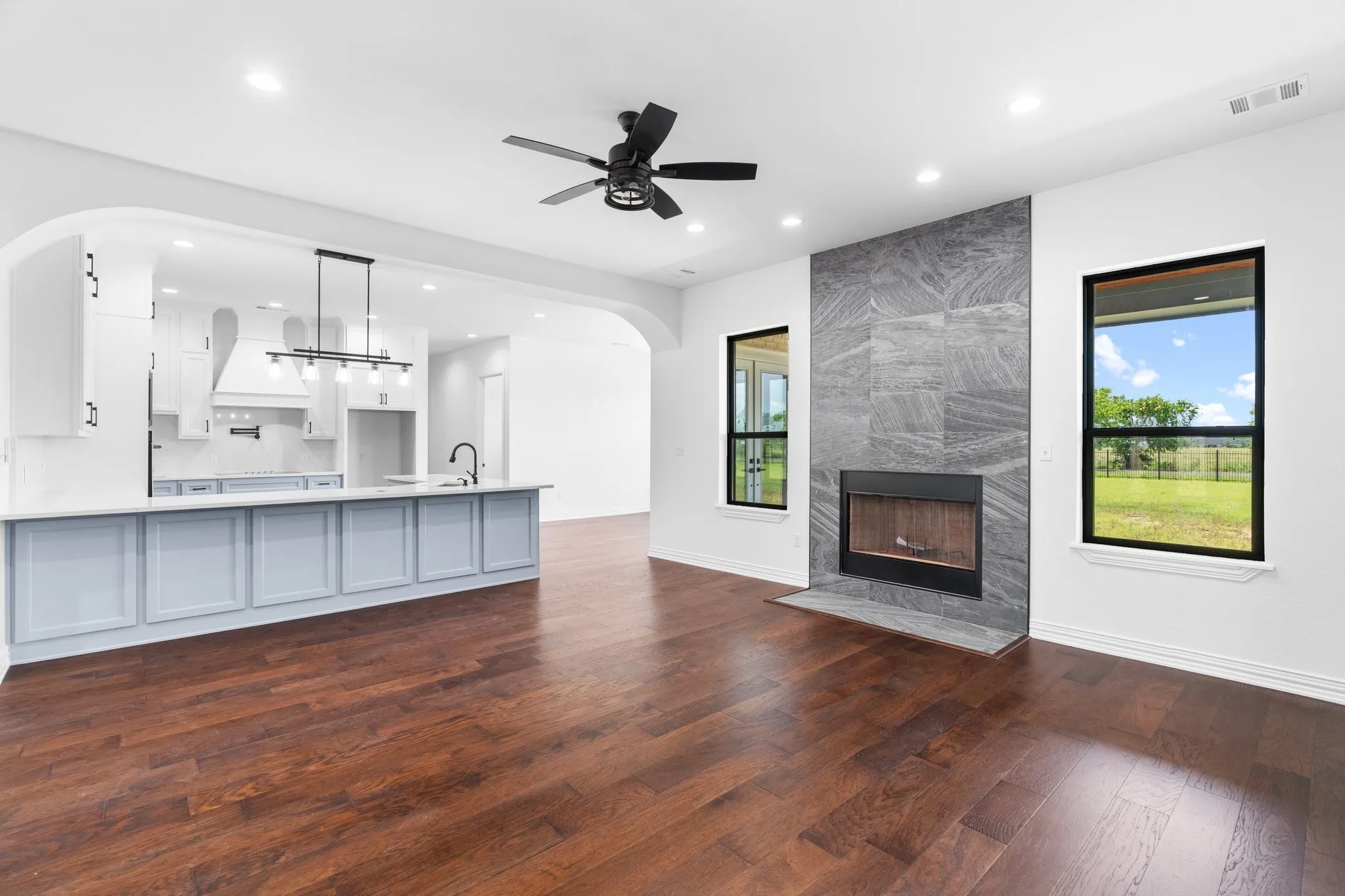 Unfurnished living room with dark wood-style flooring, recessed lighting, arched walkways, ceiling fan, and a fireplace